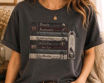 Może przedstawiać: Ciemnoszary t-shirt z nadrukiem graficznym przedstawiającym stos klasycznych książek, w tym Dracula, Frankenstein, The Raven, Wuthering Heights, The Picture of Dorian Gray, Jane Eyre, The Fall of the House of Usher oraz Les Misérables.