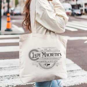 May include: A white canvas tote bag with a black and white design that says "Lady Macbeth's Cleaners, Inverness, Scotland, Spot Removal Specialists" with an illustration of a hand holding a cleaning cloth.