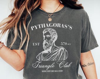 May include: Dark gray t-shirt with a white graphic of Pythagoras and the text "Pythagoras's Triangle Club" with the phrase "Where Every Side Has a Story". The shirt has a vintage, worn look.