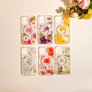 May include: Clear phone cases with embedded dried flowers in various colors, including pink, purple, yellow, and red. Each case features a circular design element. The cases are arranged in a grid, showcasing the floral arrangements.