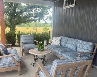 May include: A patio furniture set featuring light wood frames and blue textured cushions. The set includes a sofa, two armchairs, and a round mosaic-topped coffee table. A white throw pillow with a bird pattern sits on the sofa, and a small potted plant rests on the table under a ceiling fan.