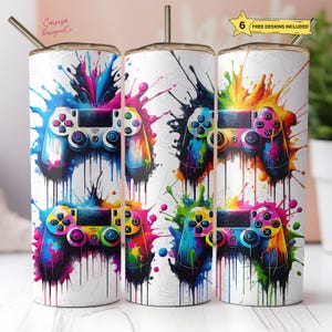 May include: White stainless steel tumblers with colourful controller designs. Each tumbler features a different controller design with vibrant paint splatter effects. The tumblers have a straw and the text "6 FREE DESIGNS INCLUDED".