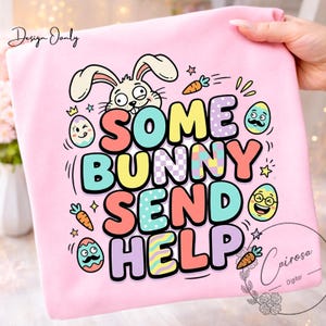 May include: A light pink sweatshirt with the phrase "SOME BUNNY SEND HELP" in colorful bubble letters. The design includes a cartoon bunny, Easter eggs, carrots, and stars, perfect for Easter.