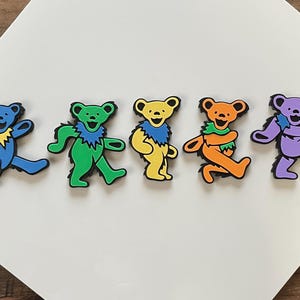 May include: Five colorful dancing bear figurines. The bears are in various poses and are made of a rubbery material. The bears are blue, green, yellow, orange, and purple.