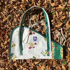 Może przedstawiać: Ręcznie robiona torba typu tote z białym tłem i kwiatowym wzorem w kolorze czerwonym, żółtym i zielonym. Torba ma zielone wykończenia i uchwyty, z napisem "what i" z przodu.