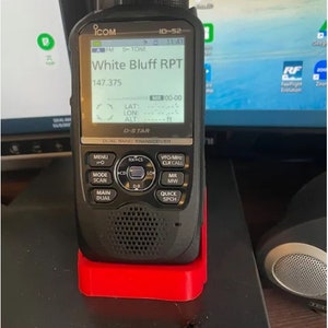 May include: A black handheld radio with a red base. The radio screen displays "White Bluff RPT" and "147.375". The radio has a D-STAR logo and the text "Dual Band Transceiver".