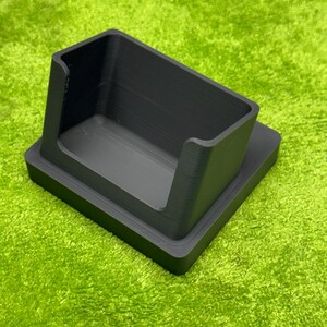 Puede incluir: Un organizador de escritorio negro, rectangular, con un compartimento elevado con la parte superior abierta. El organizador se asienta sobre una base plana y está hecho de un material mate. El diseño es simple y moderno, adecuado para la oficina o el hogar.