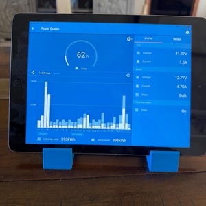 May include: A tablet displaying the "Power Queen" app interface, showing solar power output of 62W and various voltage and current readings. The screen displays a graph of energy production over time. The tablet is supported by two small, blue stands.
