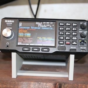 May include: A black Uniden SDS200 digital scanner radio with a large color display showing text including Tennessee Advanced Communications, TGID 47088, and Charlotte. The device features a silver volume knob, a numeric keypad, and ports.