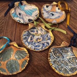 May include: Five decorative seashells with gold trim and blue and white painted designs. Each shell has a ribbon attached for hanging.