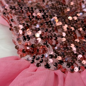 May include: Pink tulle dress with a sequined bodice. The bodice is covered in copper-colored sequins, and the skirt is made of layers of soft pink tulle. A delicate, feminine garment.