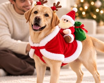 May include: A yellow Labrador retriever wearing a red and white Santa Claus costume with a plush Santa figure attached to the back, a green gift sack, and a brown reindeer antler headband with small red pom-poms on the dog's head.