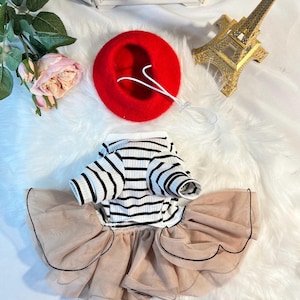 Pu&ograve; includere: Una camicia a righe bianche e nere con una gonna di tulle beige e un berretto rosso. L'abito &egrave; progettato per un cane di piccola taglia.