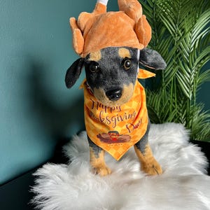 May include: A black and brown dog wearing a brown turkey costume and a yellow bandana with the text "Happy Thanksgiving Day".