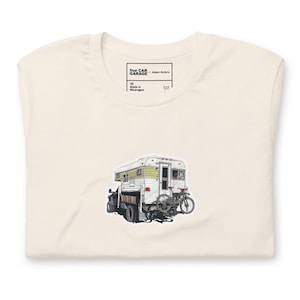 May include: Cream-colored t-shirt featuring a graphic of a camper attached to a truck, with a bicycle mounted on the back. The shirt has a tag that reads "five CAR GARAGE - Adam Ambro" and "Made in Nicaragua".
