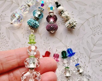 May include: A collection of beaded ornaments in various colors and designs. The ornaments feature clear, iridescent, and colorful beads, including faceted crystal and glittery spheres. Each ornament has a silver-tone loop for hanging.