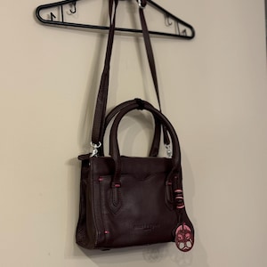 May include: A dark brown leather handbag with a top handle and a long shoulder strap. The bag has a pink leather accent and a pink metal charm.