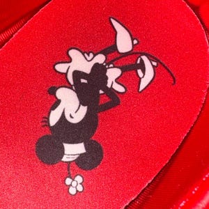 Puede incluir: Primer plano de una plantilla de zapato roja con un personaje de dibujos animados en blanco y negro sosteniendo una flor. La plantilla es roja y tiene una superficie texturizada.