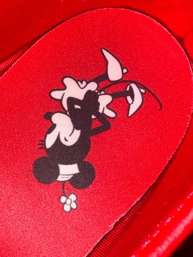 Puede incluir: Primer plano de una plantilla de zapato roja con un personaje de dibujos animados en blanco y negro sosteniendo una flor. La plantilla es roja y tiene una superficie texturizada.