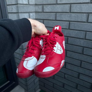 Puede incluir: Un par de zapatillas rojas con detalles y cordones blancos. Los zapatos presentan un dise&ntilde;o blanco en los laterales y un peque&ntilde;o detalle de lazo en el tal&oacute;n. Las suelas son rojas.