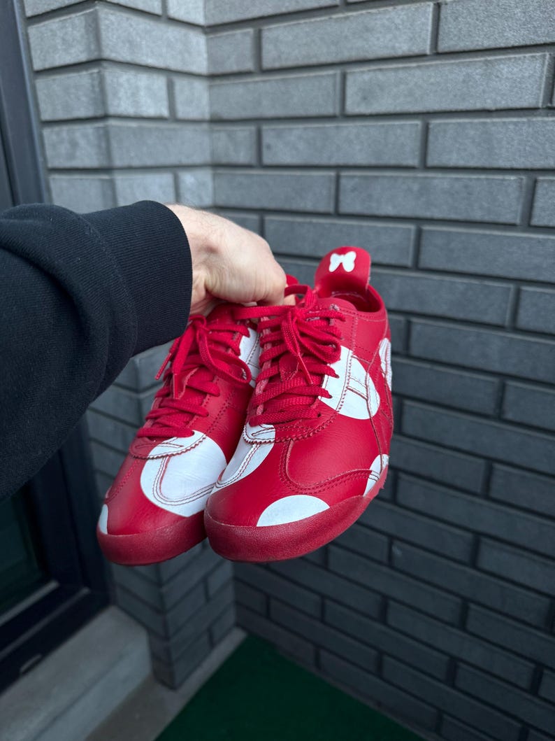 Puede incluir: Un par de zapatillas rojas con detalles y cordones blancos. Los zapatos presentan un dise&ntilde;o blanco en los laterales y un peque&ntilde;o detalle de lazo en el tal&oacute;n. Las suelas son rojas.
