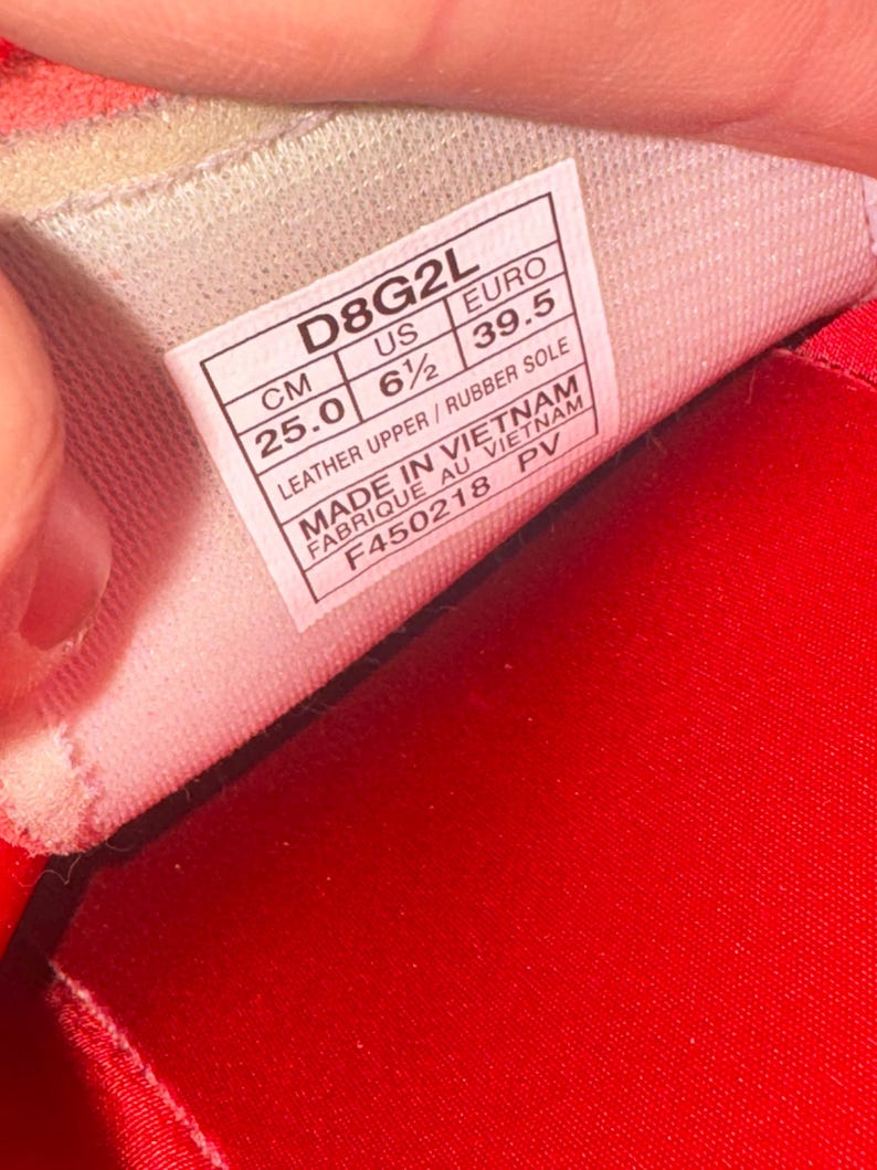 Puede incluir: Primer plano del interior de un zapato, con una etiqueta blanca y texto negro. La etiqueta indica una talla de 39,5 y una medida de 25,0 cm. El zapato es rojo.