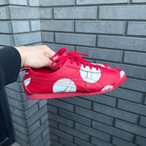 Puede incluir: Zapatilla deportiva roja con lunares blancos y rayas blancas. La zapatilla tiene cordones rojos y suela roja. La zapatilla es de cuero y tiene un dise&ntilde;o cl&aacute;sico.