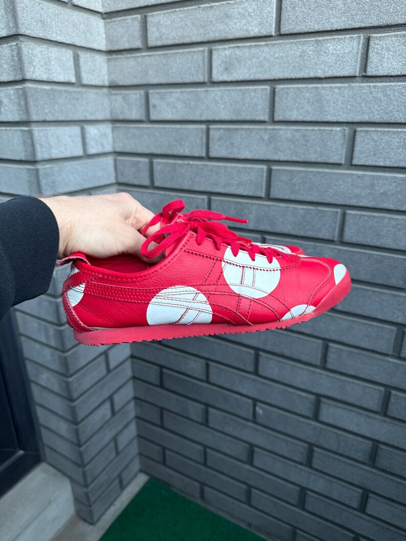 Puede incluir: Zapatilla deportiva roja con lunares blancos y rayas blancas. La zapatilla tiene cordones rojos y suela roja. La zapatilla es de cuero y tiene un dise&ntilde;o cl&aacute;sico.