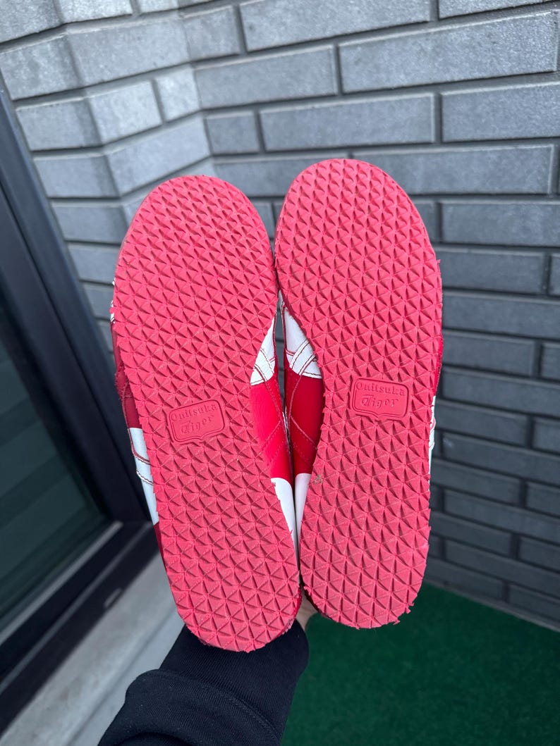 Puede incluir: Par de zapatillas deportivas rojas y blancas, vistas desde las suelas. Las suelas son de goma roja texturizada con un patr&oacute;n repetitivo. Rayas blancas y el nombre de la marca son visibles en los laterales.