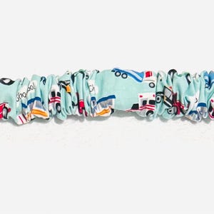 May include: A light blue dog collar with a repeating pattern of various vehicles, including ambulances, planes, and buses. The collar has a green plastic buckle and a metal ring. The text "Choo Choo!" is visible on the collar.