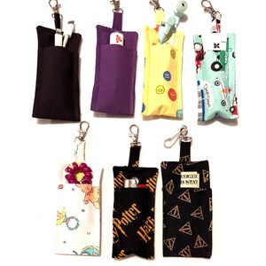 May include: Seven rectangular fabric pouches with metal lobster claw clasps. The pouches feature various patterns including solid black, solid purple, yellow with buttons, light blue with trains, white with baby items, black with Harry Potter text, and black with gold symbols.