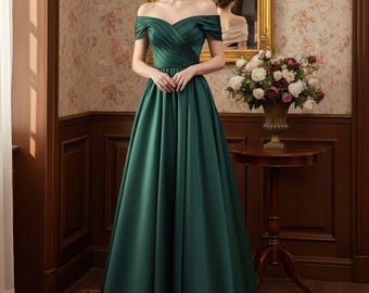 Peut inclure: Une robe de soirée émeraude à épaules dénudées. La robe présente un corsage plissé et une jupe évasée fluide. La femme se tient dans une pièce avec du papier peint floral et un miroir doré.