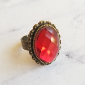 May include: A red gemstone ring with an ornate bronze setting. The ring has a detailed design with small beads around the edge of the setting.