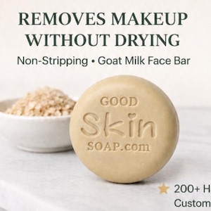 May include: A round, beige goat milk face bar with the embossed text GOOD Skin SOAP.com. Above the soap, the text reads REMOVES MAKEUP WITHOUT DRYING and Non-Stripping • Goat Milk Face Bar. A small bowl of oats sits behind the soap, and a star icon with 200+ Happy Customers is visible.