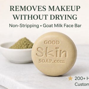 May include: A round, light-colored goat milk face bar with the text "GOOD Skin SOAP.com" is displayed. The image also shows a small white bowl with a pile of green powder and the text "REMOVES MAKEUP WITHOUT DRYING".