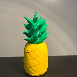 May include: A 3D printed pineapple with a yellow body and green leaves. The pineapple is a decorative object.