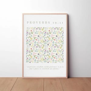 May include: A framed print featuring the text "PROVERBS 19:11" above a floral pattern. The floral design includes various pastel-colored flowers and greenery on a cream background. The quote "A person's wisdom yields patience; it is to one's glory to overlook an offense" is below.