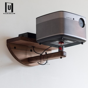 May include: A silver and black projector mounted on a wooden bracket. The bracket is made of dark wood and has a curved design. The projector has a mesh speaker cover and a red adjustment knob.
