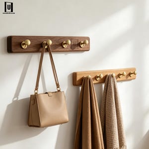 May include: Two wooden coat racks with brass hooks mounted on a white wall. One rack is holding a tan handbag, the other is holding two scarves. The racks are made of dark and light wood.
