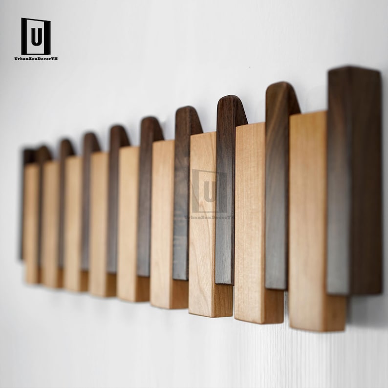May include: A modern wooden wall-mounted coat rack with alternating light and dark wood panels. The rack features a series of vertical rectangular pieces, creating a stylish and functional storage solution. The design is minimalist and contemporary.