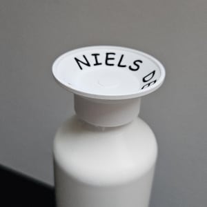 Op de afbeelding: Witte fles met een blauwe bodem en een witte dop. De dop heeft de tekst "NIELS" erop.