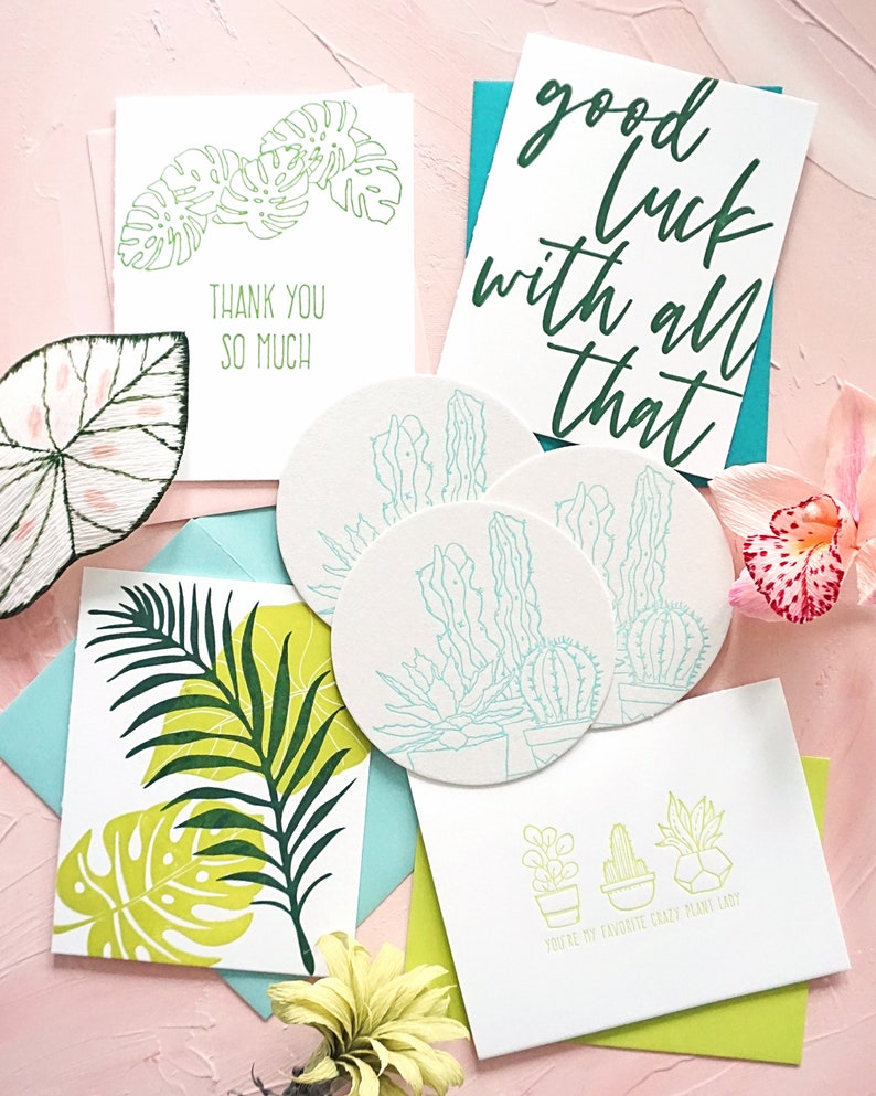 May include: A collection of greeting cards and coasters with botanical designs. The cards feature phrases like "Thank You So Much" and "Good Luck With All That." The coasters and cards have illustrations of plants and cacti.