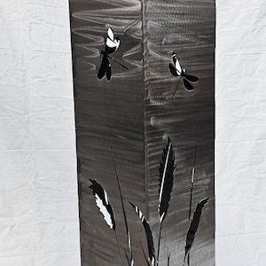 May include: A metal garden sculpture with a square base and a tall rectangular column. The column is decorated with cut-out designs of dragonflies and tall grasses.