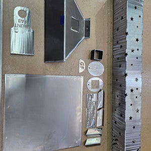 May include: A collection of metal cutouts, including a star-shaped design, a rectangular piece with the text "GRUNT FABWORKS", and a smaller rectangular piece with the text "GF".