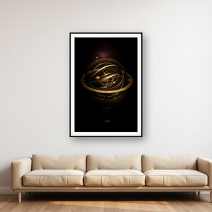 May include: A framed wall art print featuring a gold-toned armillary sphere against a deep black background. The spherical instrument consists of multiple intersecting metal rings and a central globe, displayed in a thin black frame on a white wall.