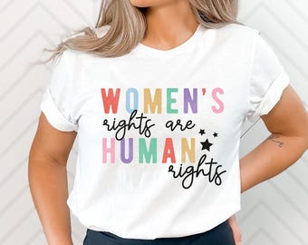 May include: White t-shirt with the text "WOMEN'S rights are HUMAN rights" in rainbow colors with black stars.