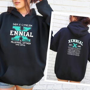 May include: Black hoodie with the text "GEN X CYNICISM ENNIAL" in white and teal. The hoodie also features the years "1977 & 1985" and the phrase "MILLENNIAL OPTIMISM AND DRIVE". The back of the hoodie has the text "XENNIAL 1977 < 1985".