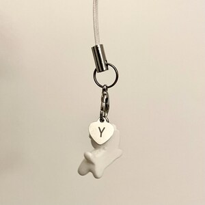 May include: White ceramic charm with a heart-shaped tag that says "Y" attached to a silver chain and a silver cord.