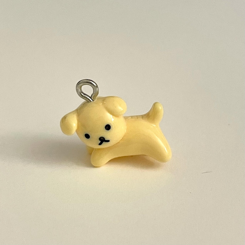 May include: A small yellow ceramic dog charm with black eyes and a silver jump ring.