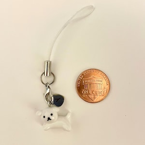 May include: White ceramic dog charm with a silver clip and a silver charm with the number 7 on it. The charm is attached to a white string.